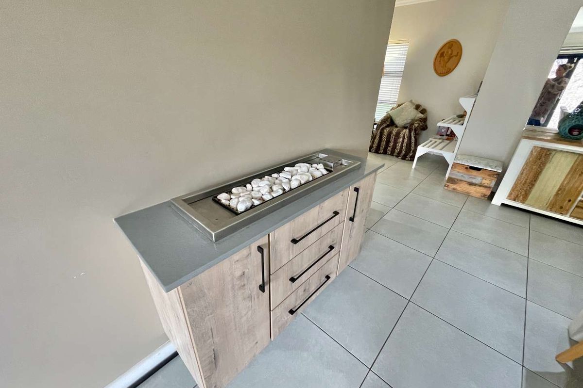 A modern built-in sideboard or console unit featuring light wood-grain cabinetry, a grey stone countertop, and an integrated decorative pebble fireplace insert.