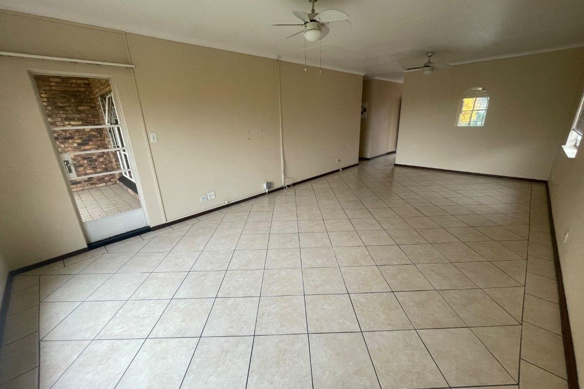Spacious, empty living area featuring neutral tiled flooring, ceiling fans, and access to an outdoor patio through a glass panel door.