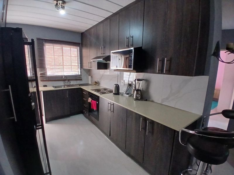 Modern kitchen featuring dark wood cabinetry, stone countertops, built-in oven, hob, and extractor fan with a clean tiled backsplash.
