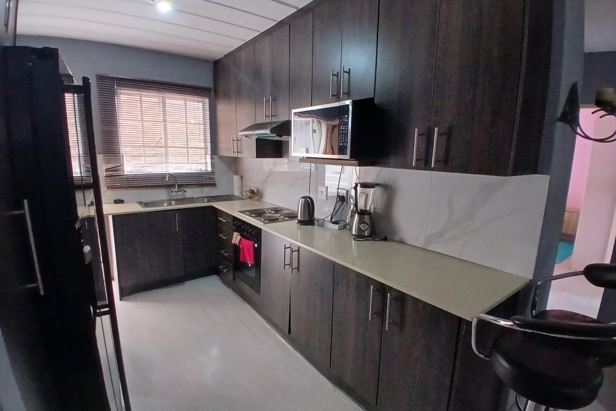 Modern kitchen featuring dark wood cabinetry, stone countertops, built-in oven, hob, and extractor fan with a clean tiled backsplash.