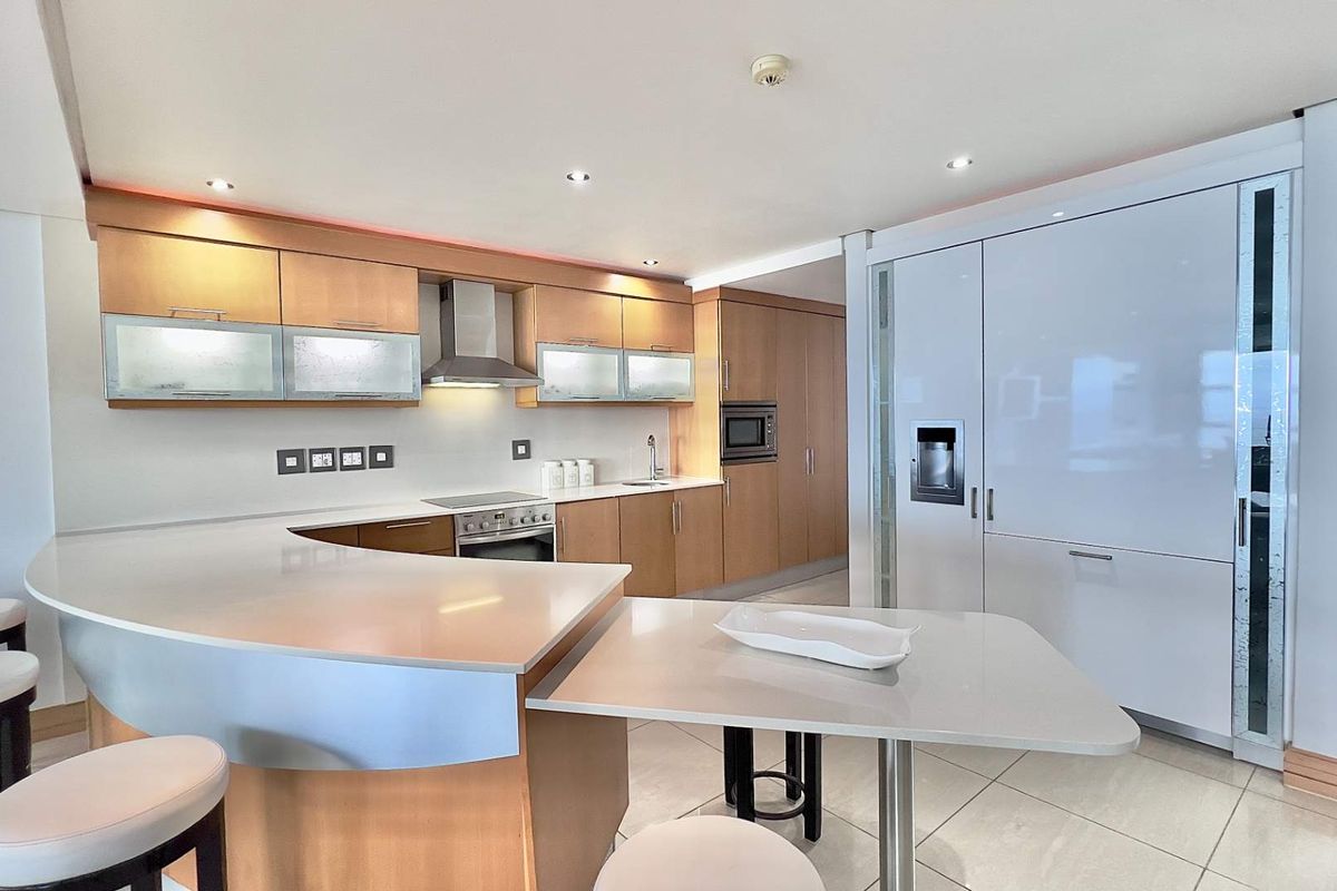 Modern kitchen featuring light wood cabinetry, integrated appliances, stone countertops, and a breakfast bar island with recessed lighting.