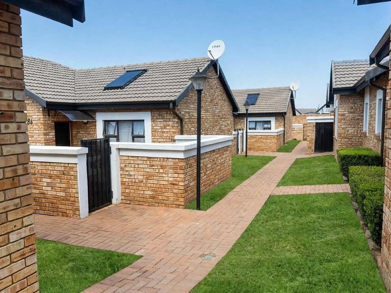 A well-maintained townhouse complex exterior featuring face brick facades, tiled roofs with solar panels, paved walkways, and neat garden areas.
