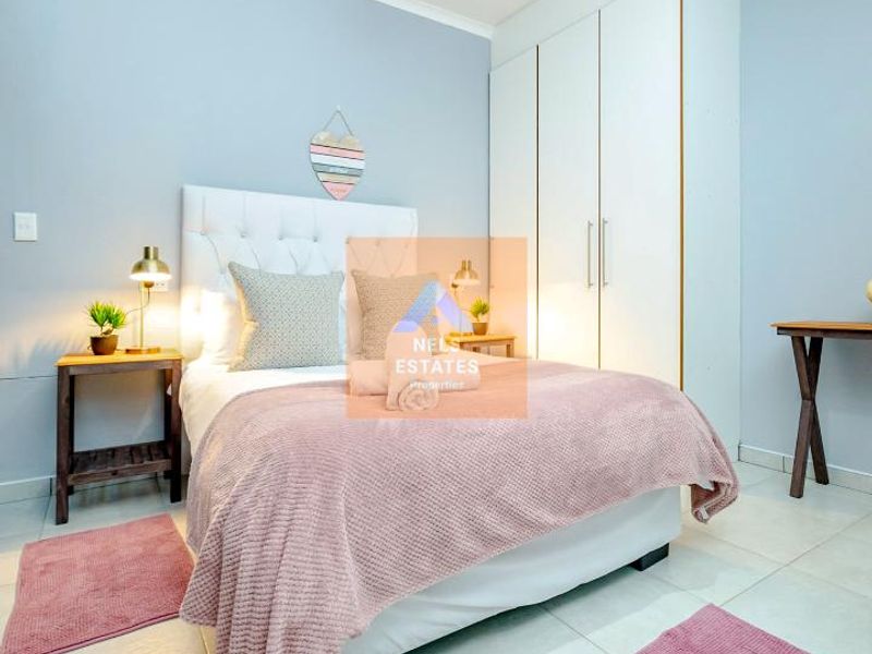 A well-maintained bedroom featuring neutral tiled flooring, built-in storage cupboards, and a modern pendant light fixture.