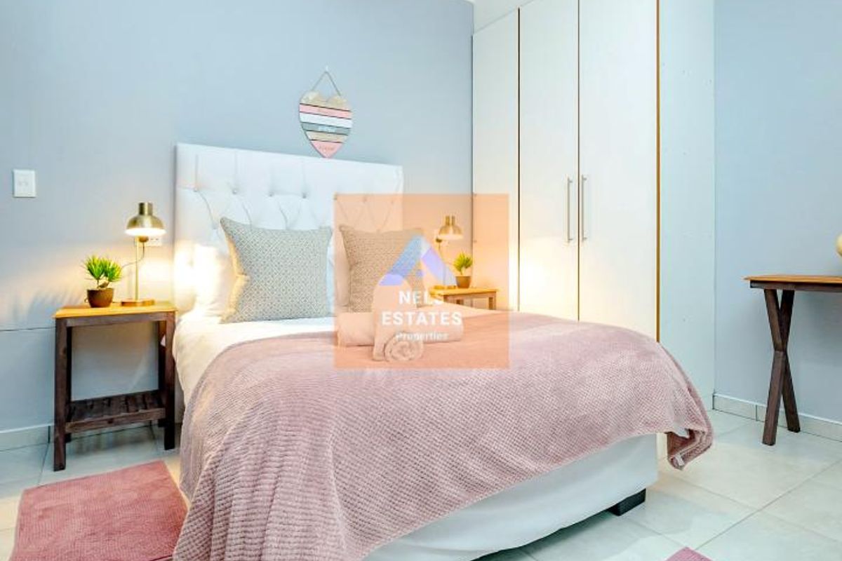 A well-maintained bedroom featuring neutral tiled flooring, built-in storage cupboards, and a modern pendant light fixture.