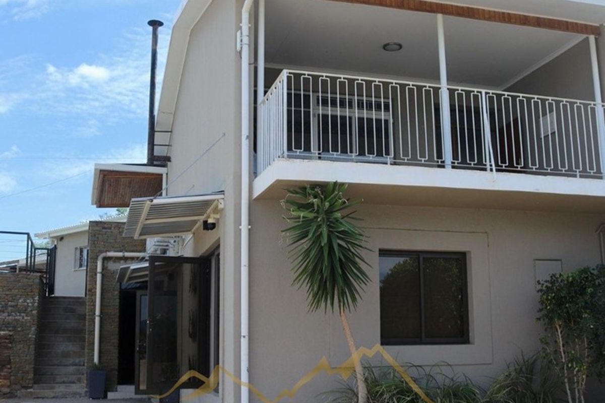 Rear exterior view of the guest house featuring a balcony with metal railing, external staircase, and stone retaining wall elements.