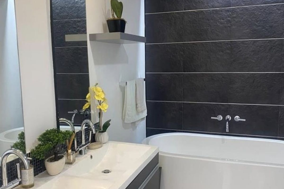 Modern bathroom featuring a sleek double vanity, a contemporary built-in bathtub, and a striking dark tiled feature wall with high-end fixtures.