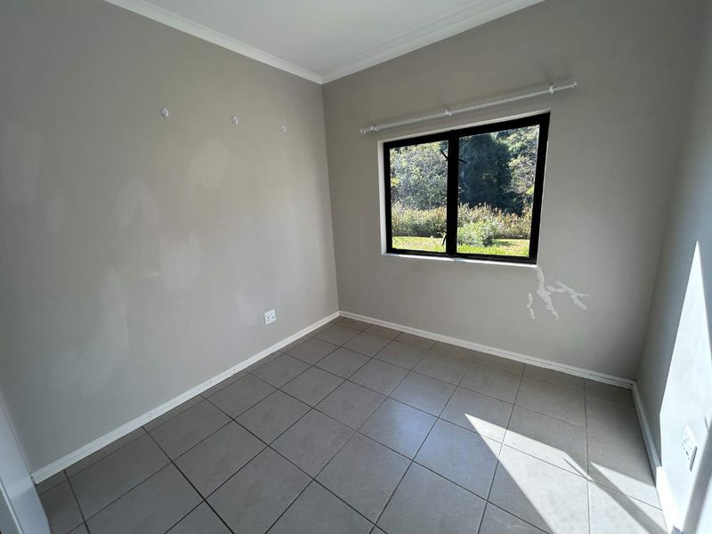 An empty bedroom featuring neutral tiled flooring, a black aluminium window frame, and walls requiring minor cosmetic repair and repainting.