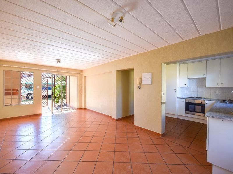 Open-plan living area and kitchen featuring tiled flooring, built-in cabinetry, and direct access to the exterior through a security gate.