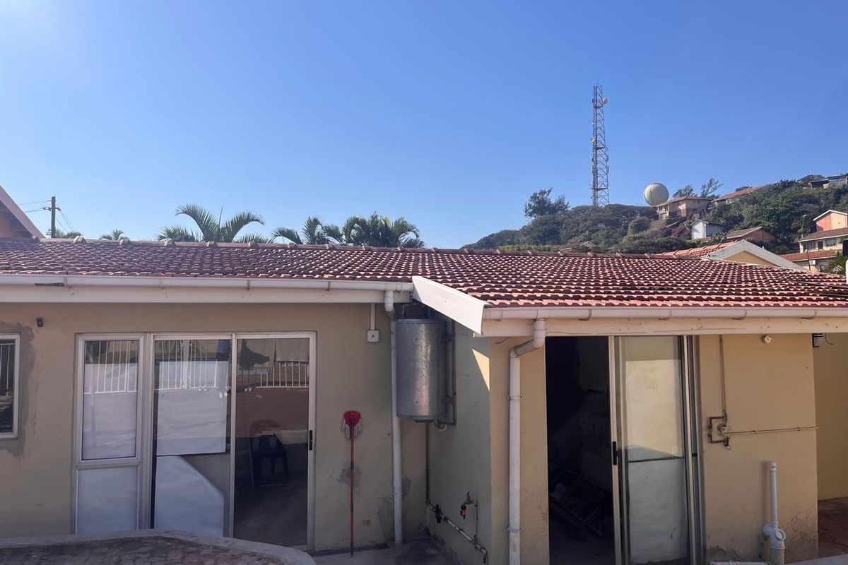 Rear exterior view of the house featuring terracotta roof tiles, aluminium sliding doors, and an external geyser unit with paved patio access.