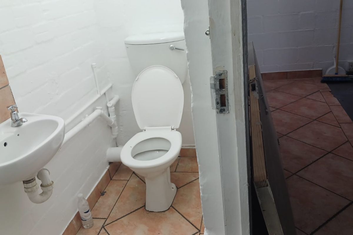 A functional bathroom featuring a toilet, wall-mounted basin, and tiled flooring, requiring cosmetic updates to improve the overall finish and aesthetic.