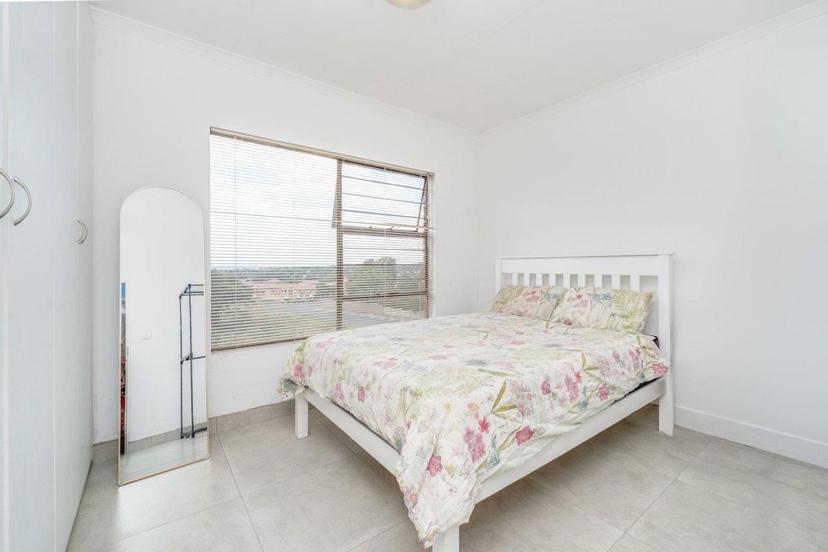 A bright bedroom featuring tiled flooring, a built-in wardrobe, and large windows with venetian blinds offering an elevated view.