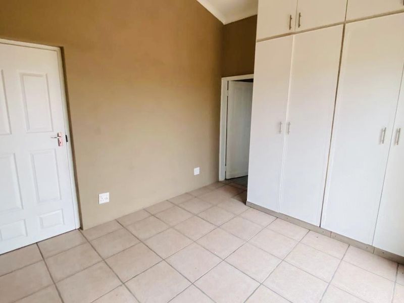 A clean, empty bedroom featuring neutral wall tones, tiled flooring, and ample built-in cupboard storage space.