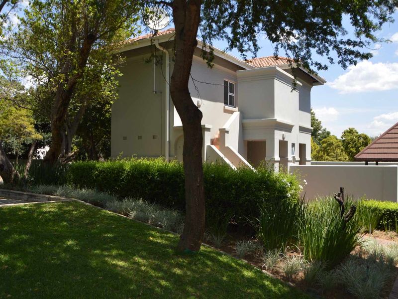 A view of the rear exterior of the apartment building, featuring a well-maintained garden, plastered walls, and a tiled roof.