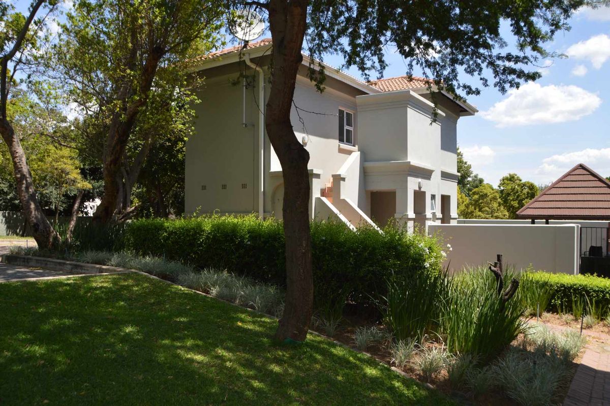 A view of the rear exterior of the apartment building, featuring a well-maintained garden, plastered walls, and a tiled roof.