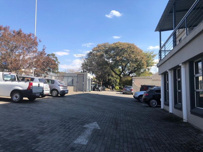Exterior view of the office property featuring a paved parking area, security gate, and building facade with a balcony.
