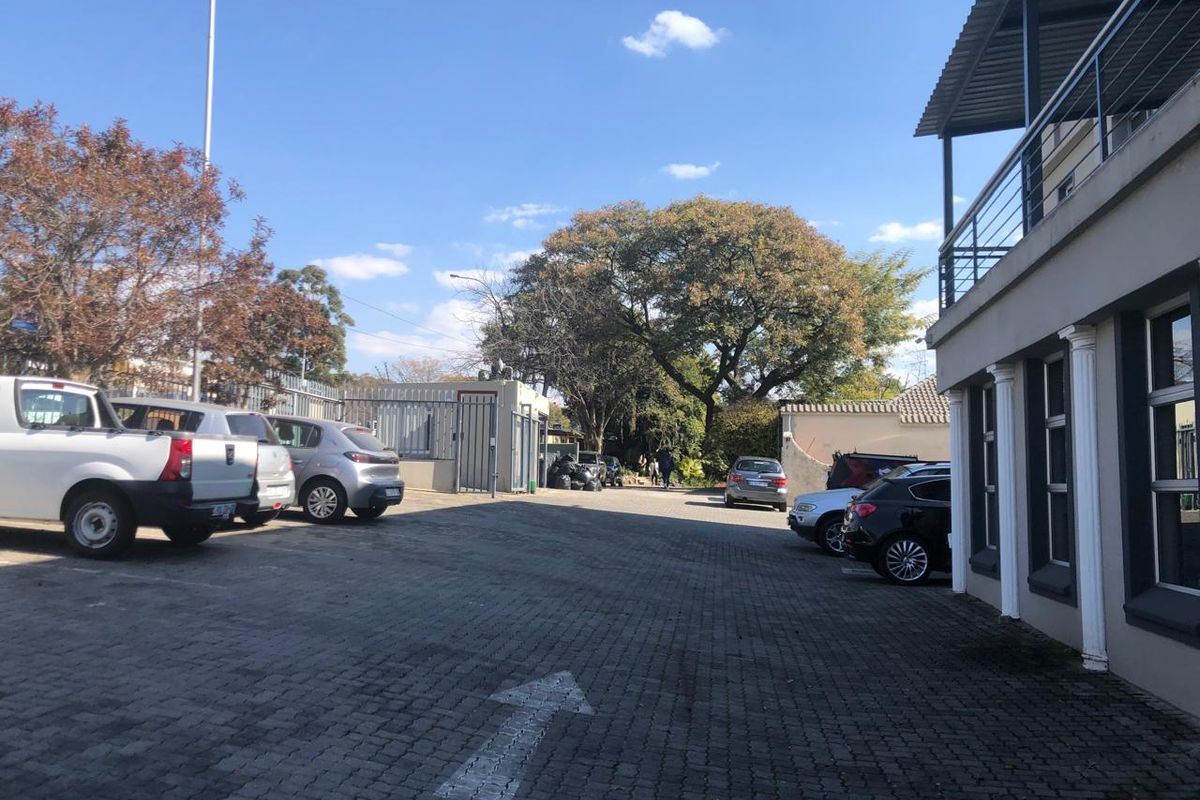 Exterior view of the office property featuring a paved parking area, security gate, and building facade with a balcony.