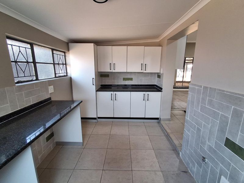 A clean, functional kitchen featuring white cabinetry, dark granite countertops, and a modern subway tile backsplash with neutral floor tiling.
