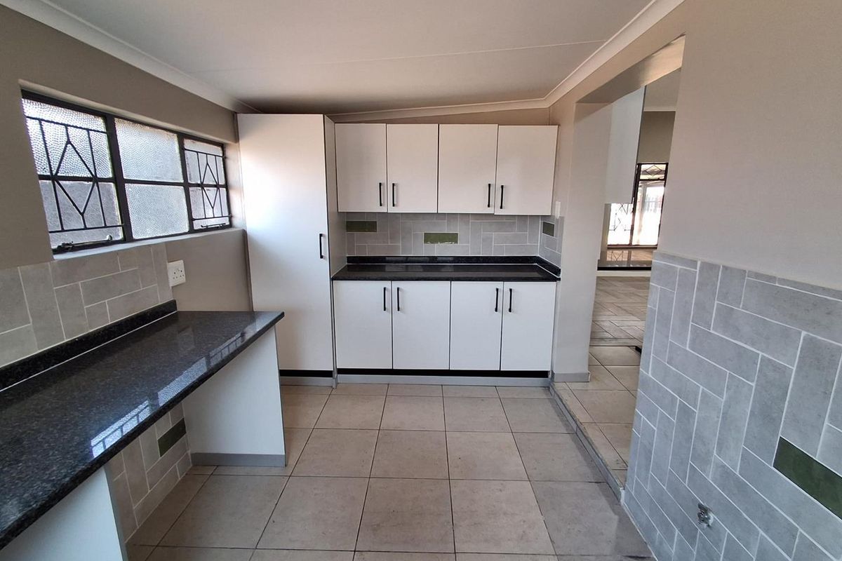 A clean, functional kitchen featuring white cabinetry, dark granite countertops, and a modern subway tile backsplash with neutral floor tiling.