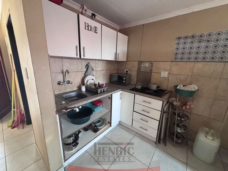 Compact kitchen featuring built-in cabinetry, a stainless steel sink, and a tiled backsplash, requiring some maintenance and cosmetic updates.