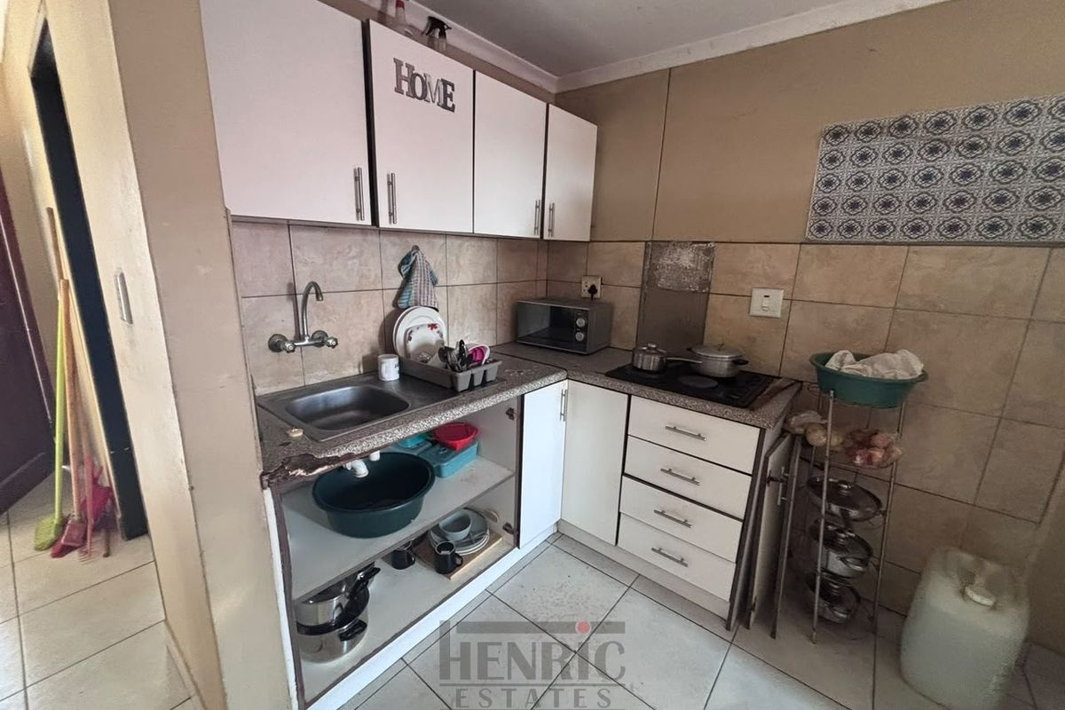 Compact kitchen featuring built-in cabinetry, a stainless steel sink, and a tiled backsplash, requiring some maintenance and cosmetic updates.