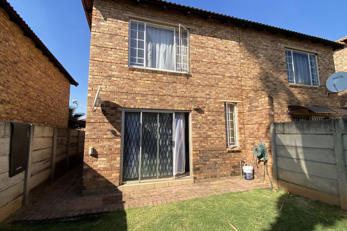 Rear view of a double-story face brick townhouse featuring a paved patio area, sliding door access, and a private garden space.