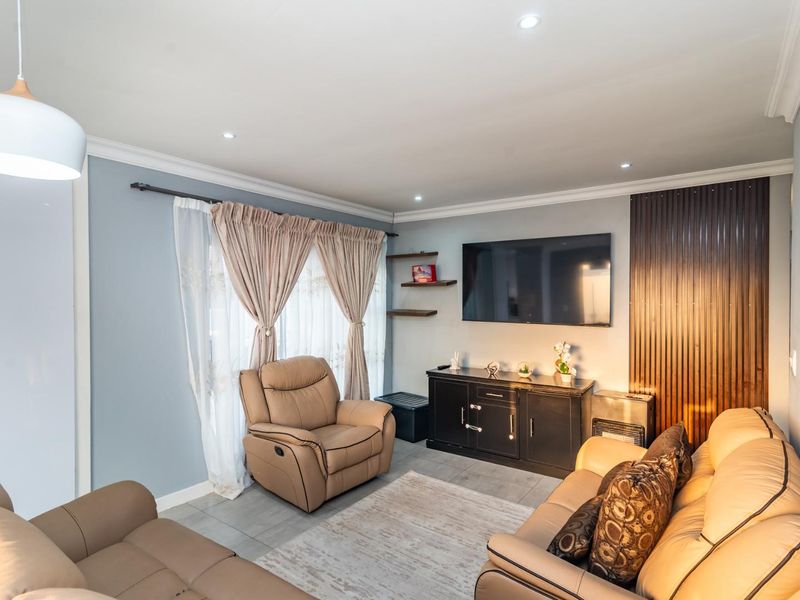 A well-maintained living room featuring tiled floors, recessed downlighting, decorative wall paneling, and floating shelves, creating a comfortable and modern living space.