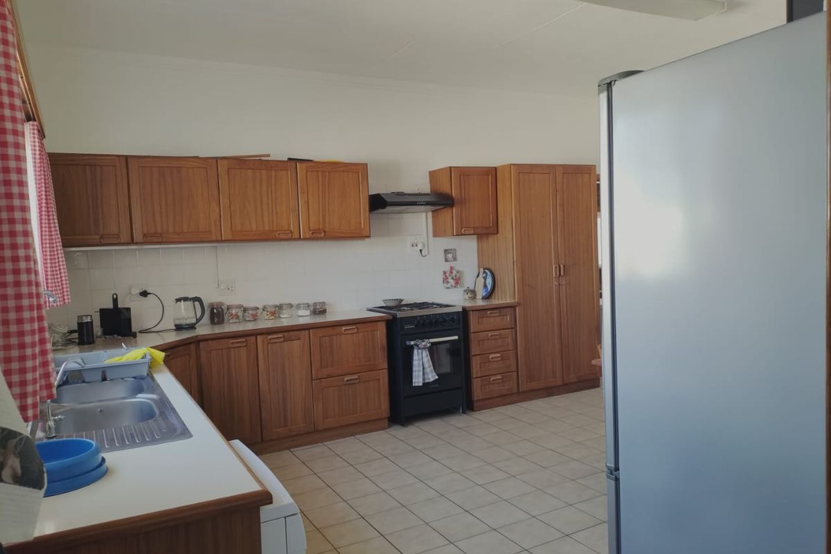 A functional kitchen featuring wooden cabinetry, a built-in oven with extractor fan, double stainless steel sink, and tiled flooring.