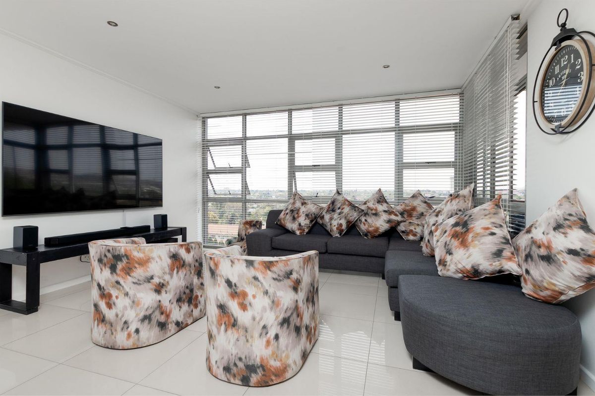 A bright and modern living room featuring large aluminium-framed windows with venetian blinds, tiled flooring, and recessed downlighting.