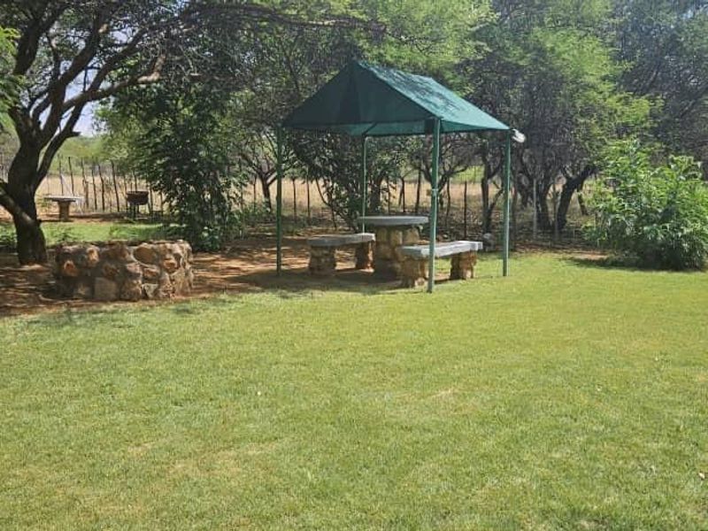 A landscaped garden area featuring a stone fire pit, a fixed gazebo with stone seating, and established trees within a fenced perimeter.