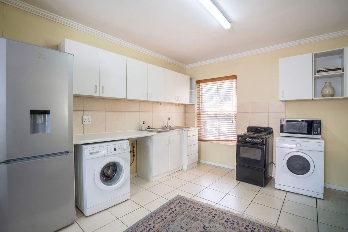 A functional kitchen featuring white cabinetry, tiled backsplash, and tiled flooring, providing a practical space for cooking and laundry tasks.