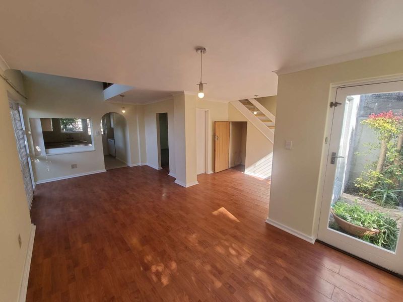 An open-plan living area featuring laminate flooring, a staircase, and a pass-through window connecting to the kitchen, with direct access to an outdoor space.