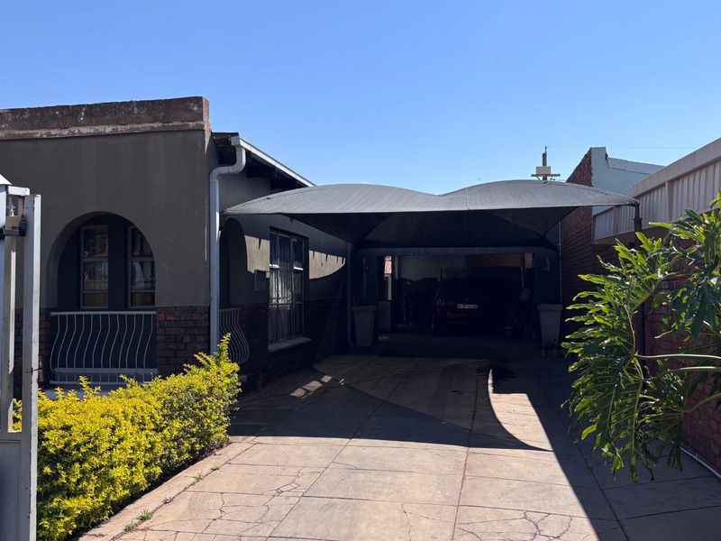 Front exterior view of the property featuring a paved driveway, shade cloth carport, and brick boundary wall.