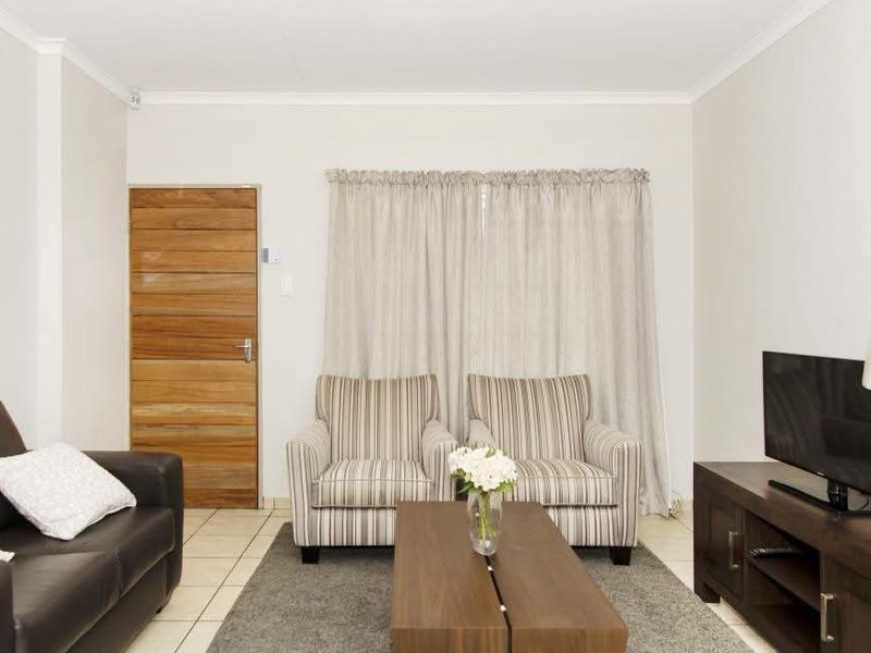 A living room featuring tiled flooring, a wooden door, and coved ceiling details, providing a functional and neutral space.