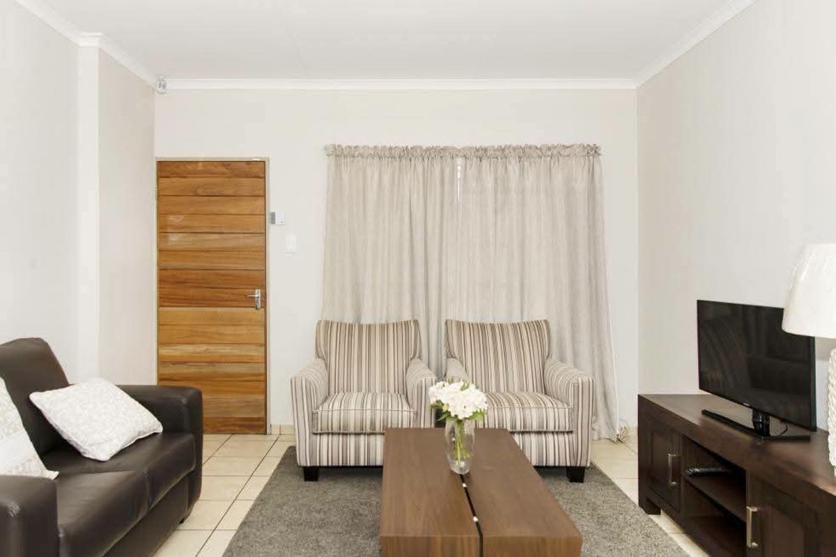 A living room featuring tiled flooring, a wooden door, and coved ceiling details, providing a functional and neutral space.