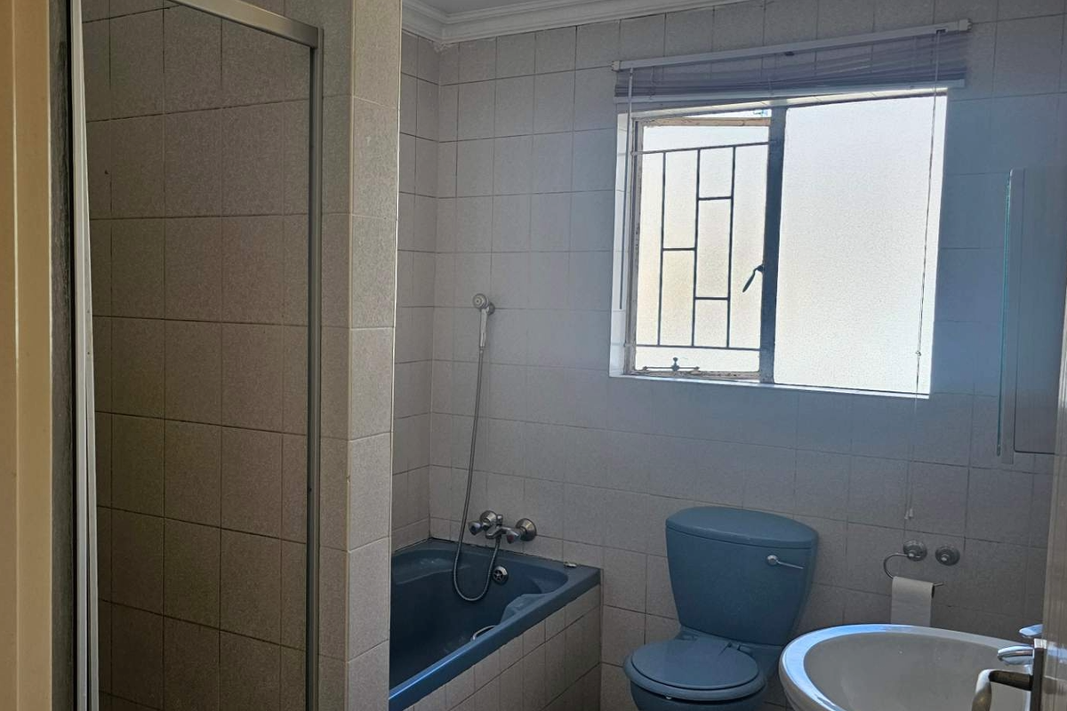 A dated bathroom featuring a blue bathtub and toilet suite, tiled walls, and a shower enclosure with a window.