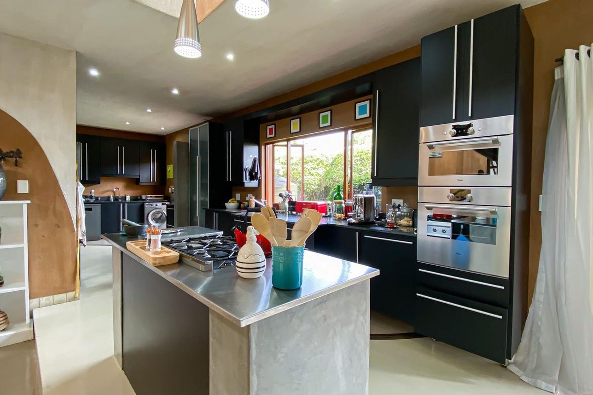 Modern kitchen featuring dark cabinetry, stainless steel built-in oven and microwave, central island with gas hob, and integrated laundry area.