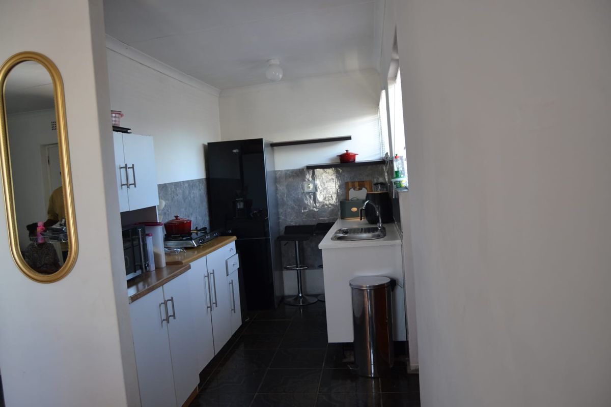 A functional galley-style kitchen featuring white cabinetry, dark tiled flooring, a built-in hob, and a stainless steel sink with a tiled backsplash.