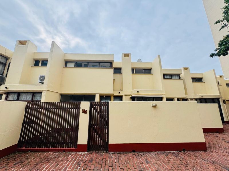 Front elevation of a multi-level apartment complex featuring a private gated entrance, brick paved driveway, and exterior wall finishes.