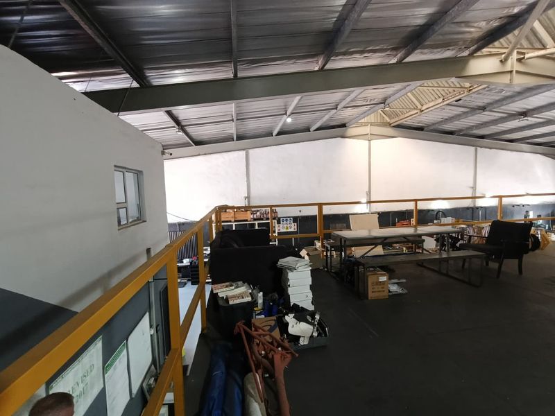 An elevated mezzanine level within an industrial warehouse space, featuring exposed steel roof trusses and safety railings.