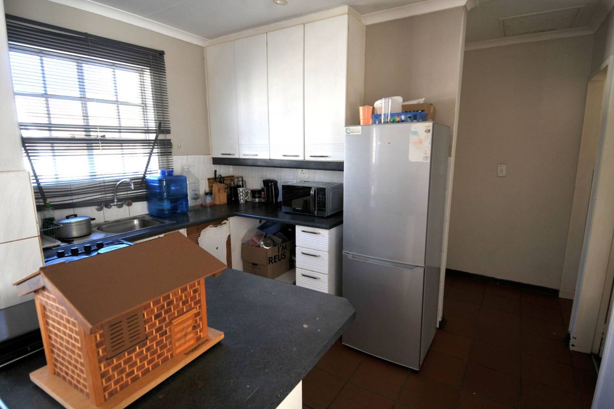 A functional kitchen featuring white cabinetry, dark countertops, a stainless steel sink, and tiled flooring, offering a practical layout for daily meal preparation.