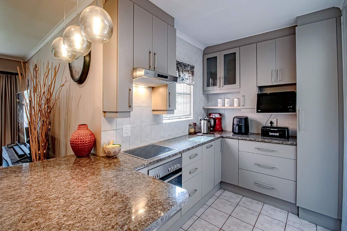 Modern kitchen featuring granite countertops, grey cabinetry, built-in oven, glass cooktop, and an integrated extractor fan with pendant lighting.