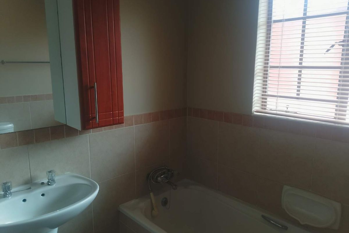 A functional bathroom featuring a pedestal basin, a bathtub with wall-mounted fixtures, and a wall-mounted vanity cabinet with neutral wall tiling.