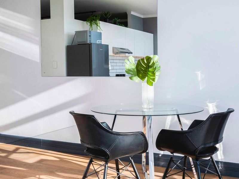 Modern open-plan living area featuring laminate flooring, crisp white walls, and a view through to a contemporary kitchen with subway tile backsplash.