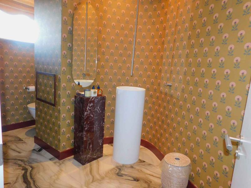 A unique bathroom featuring bold patterned wallpaper, marble-effect flooring, and a modern pedestal washbasin with a wall-mounted mirror.