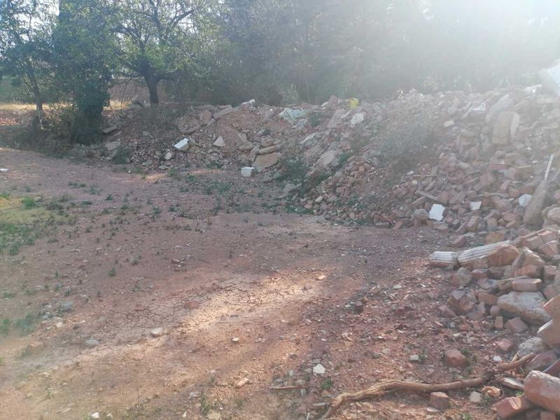 A vacant residential plot featuring a large pile of construction rubble and debris, requiring site clearing and preparation for development.