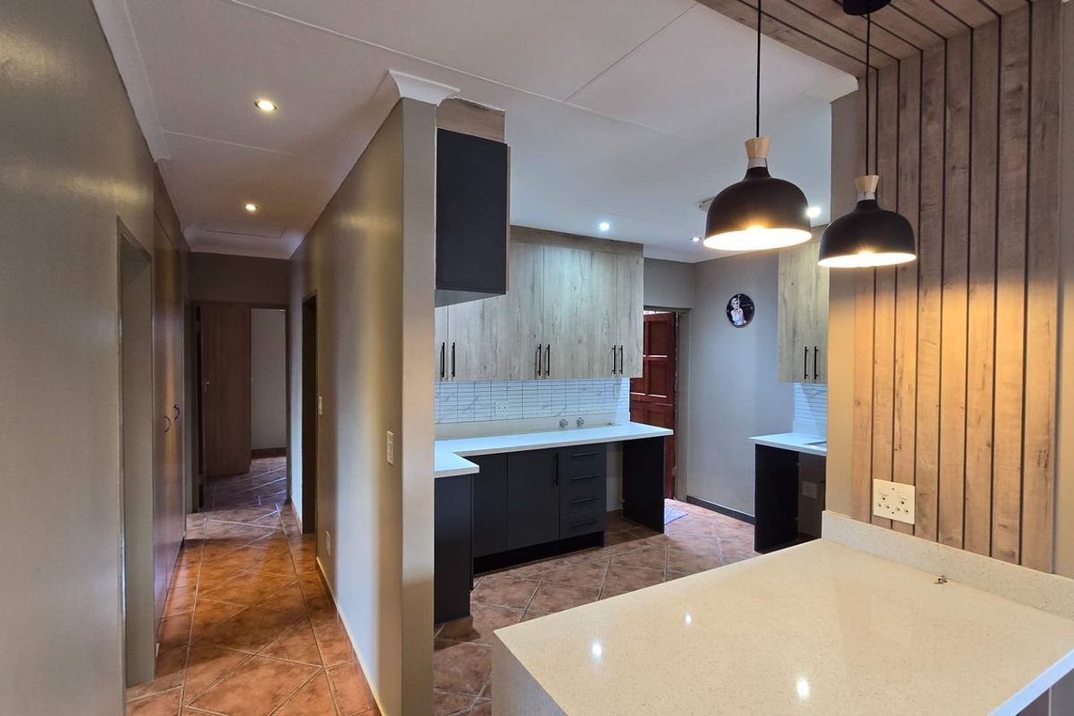 Modern kitchen featuring two-tone cabinetry, stone countertops, tiled flooring, and decorative timber wall paneling with pendant lighting.