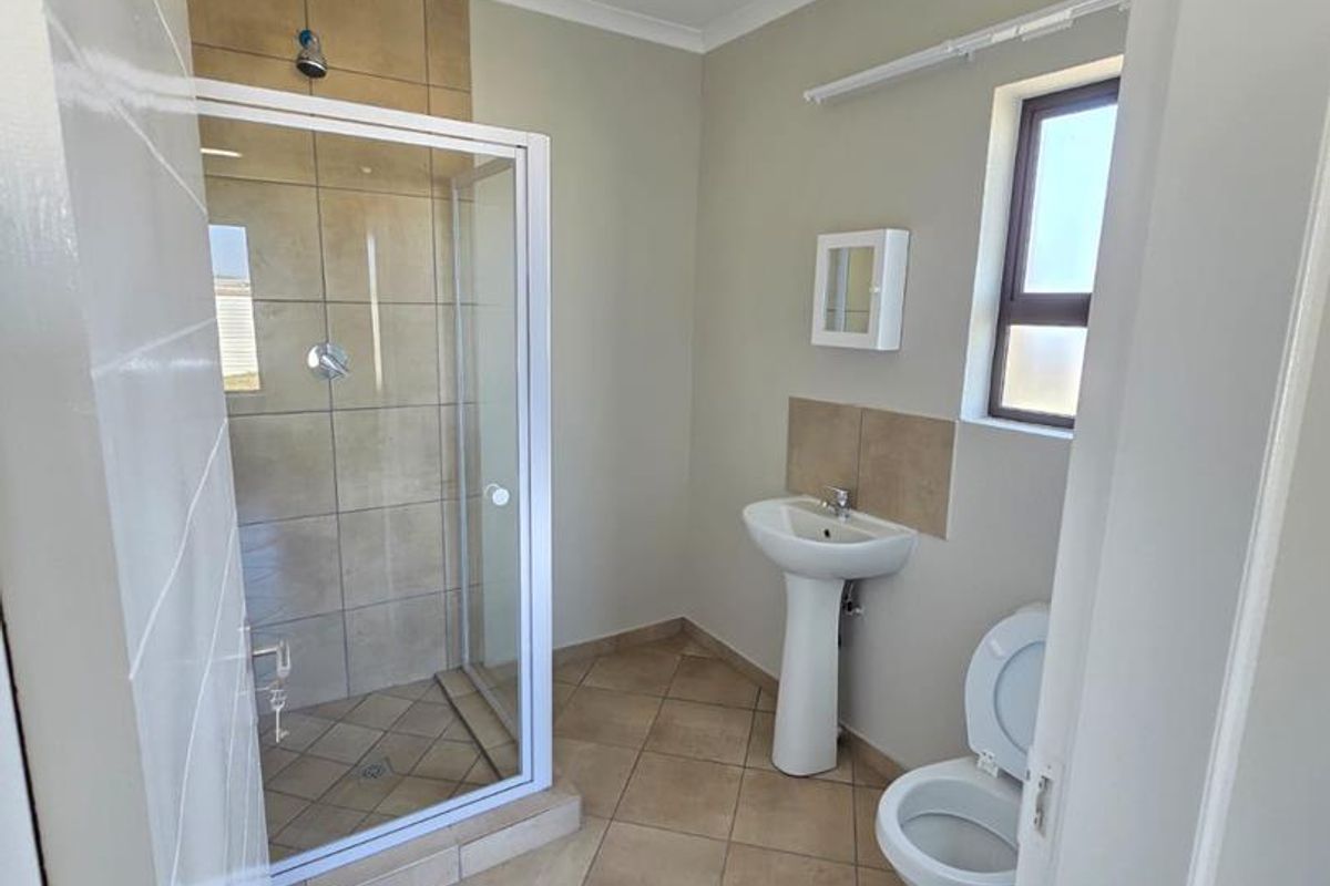 A functional bathroom featuring a tiled shower enclosure, pedestal basin, and toilet with neutral wall finishes and tiled flooring.