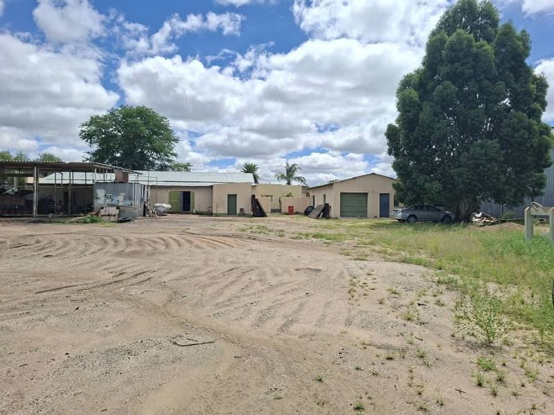 Rear view of the industrial property featuring multiple outbuildings, metal roofing, and a large unpaved yard area.