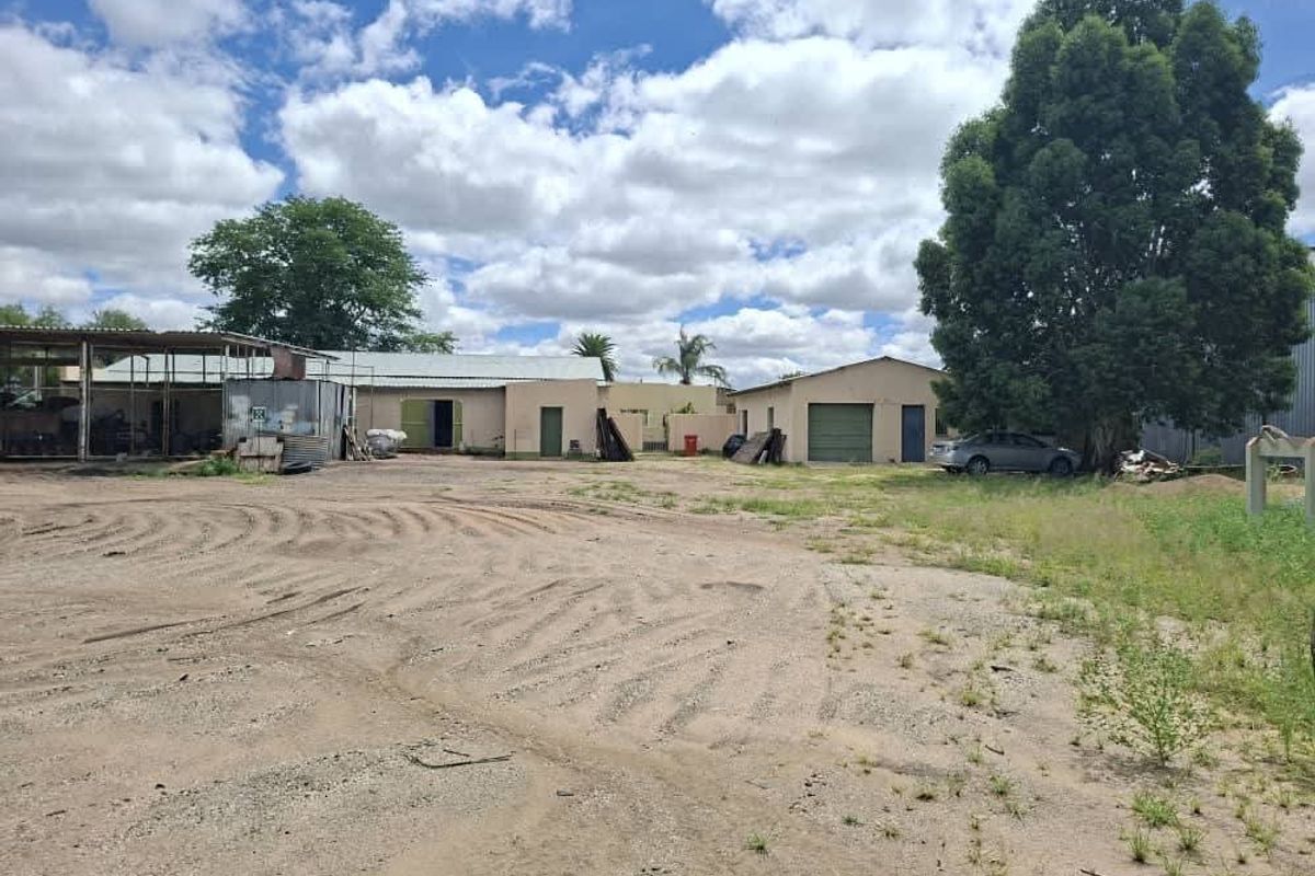 Rear view of the industrial property featuring multiple outbuildings, metal roofing, and a large unpaved yard area.