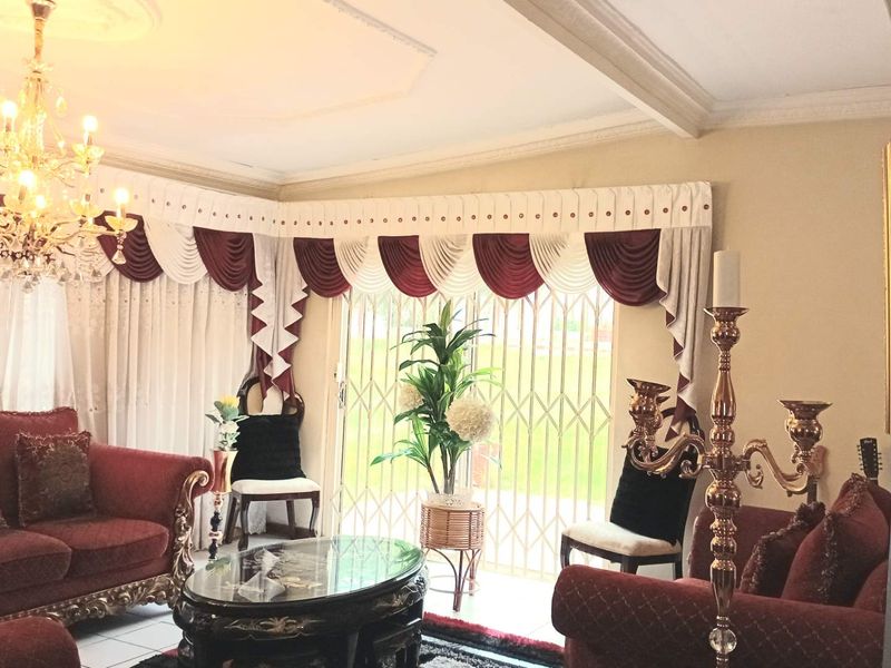 A formal living room featuring a crystal chandelier, decorative ceiling molding, and a sliding glass door with a security gate leading outdoors.